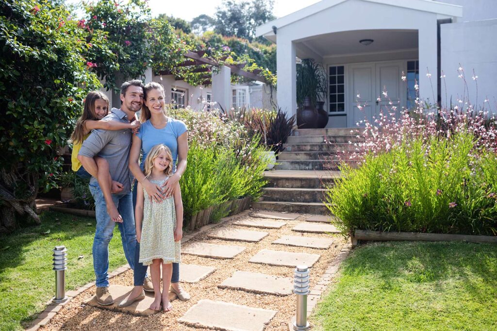 Family standing in front of home taking a portrait photo